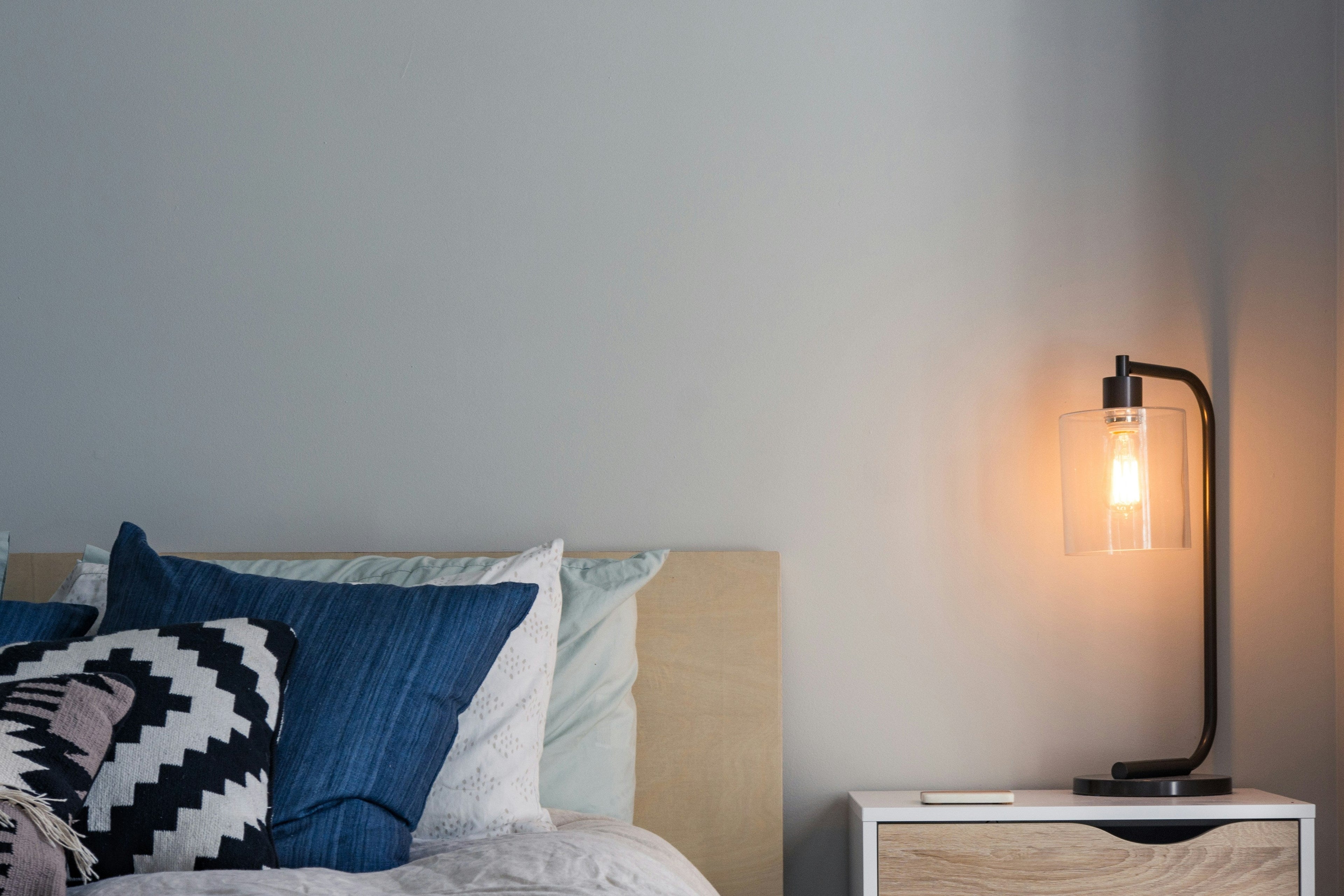 Bedroom with a bed, nightstand, and lamp against a gray wall.